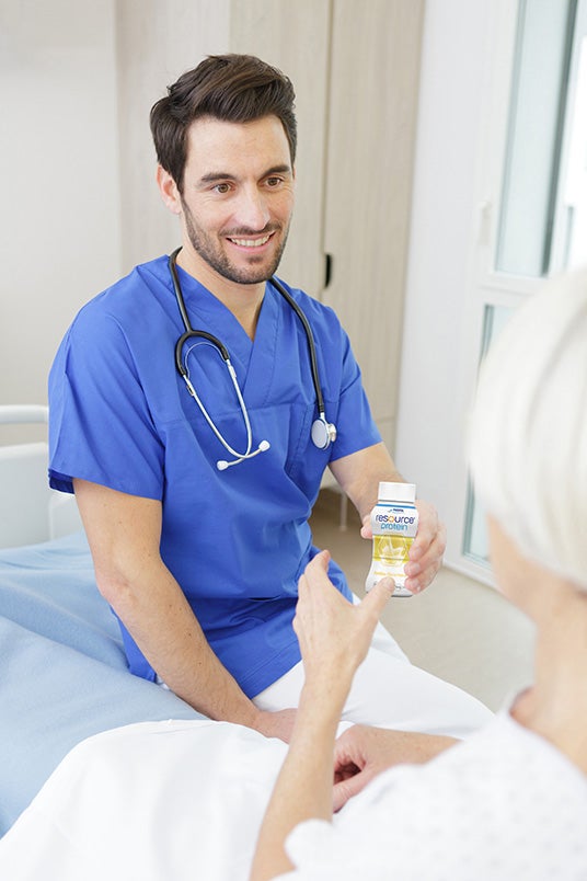 Happy hospital nurse gives cancer patient resource drinking food