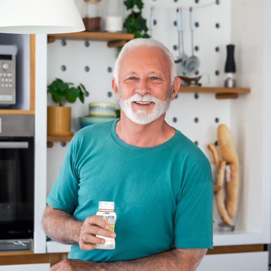 Senior in the kitchen, holds a bottle of resource drinking food in hand