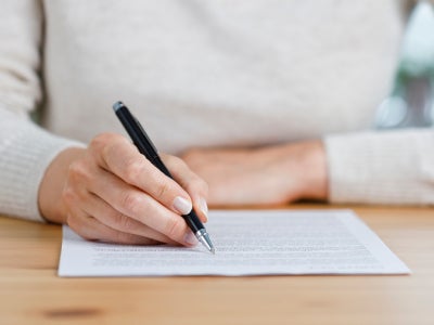 Person unterschreibt ein Dokument mit einem schwarzen Stift.