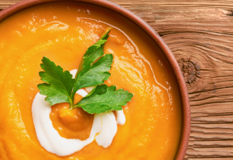 Schüssel mit cremiger Karottensuppe, garniert mit Sahne und Petersilienblatt.